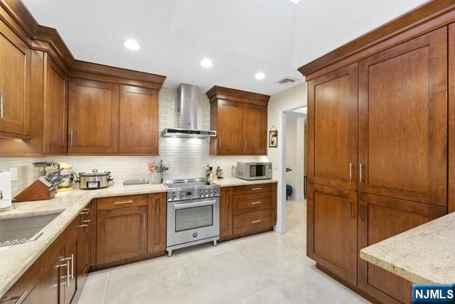 kitchen featuring decorative backsplash, recessed lighting, wall chimney exhaust hood, light stone counters, and stainless steel appliances