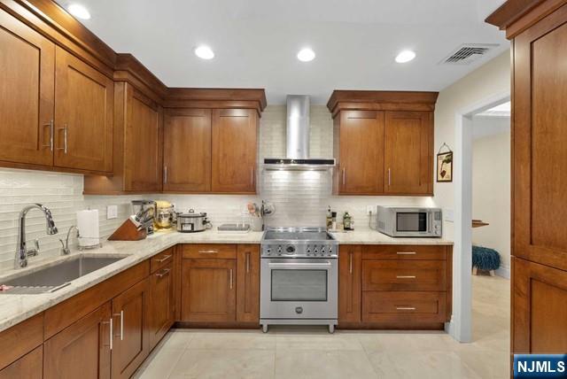 kitchen with visible vents, wall chimney range hood, tasteful backsplash, a sink, and stainless steel appliances