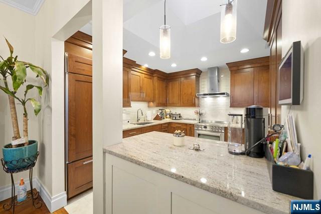kitchen with wall chimney exhaust hood, light stone counters, a sink, backsplash, and stainless steel range with electric cooktop