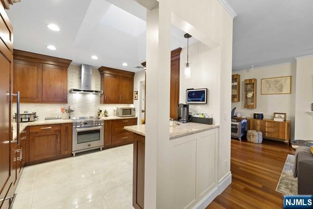 kitchen with backsplash, pendant lighting, brown cabinets, stainless steel appliances, and wall chimney exhaust hood