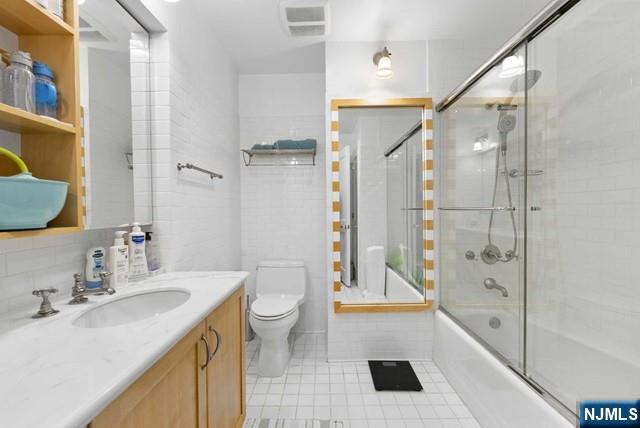bathroom featuring visible vents, tile patterned floors, vanity, toilet, and enclosed tub / shower combo