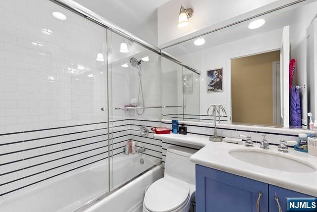 full bathroom featuring vanity, enclosed tub / shower combo, and toilet