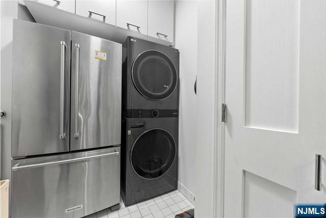 laundry area with light tile patterned floors and stacked washer / dryer