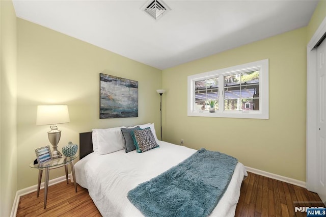 bedroom featuring baseboards, a closet, wood finished floors, and visible vents