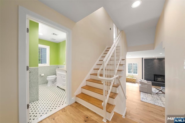 staircase with tile walls, a fireplace, wood finished floors, and visible vents