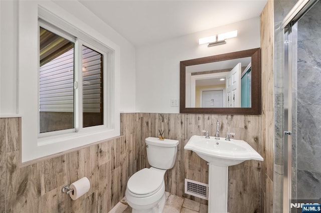 bathroom featuring tile walls, wainscoting, toilet, and visible vents