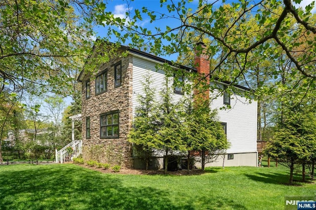 view of side of property featuring a yard, a chimney, and stone siding