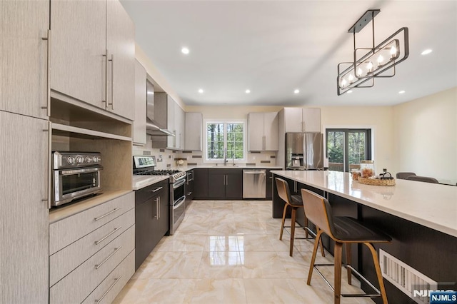 kitchen featuring wall chimney range hood, a kitchen breakfast bar, appliances with stainless steel finishes, light countertops, and marble finish floor
