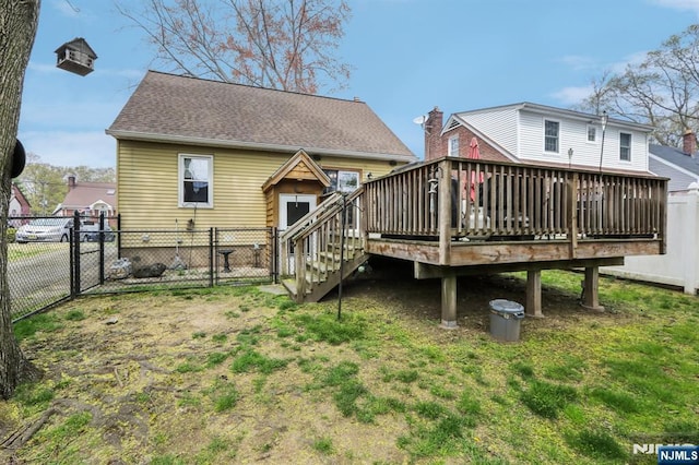 rear view of house featuring a fenced backyard, a gate, a wooden deck, and a lawn