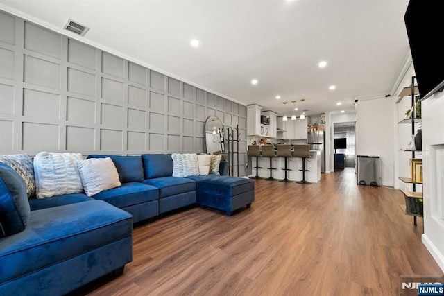 living room with crown molding, a decorative wall, wood finished floors, and visible vents