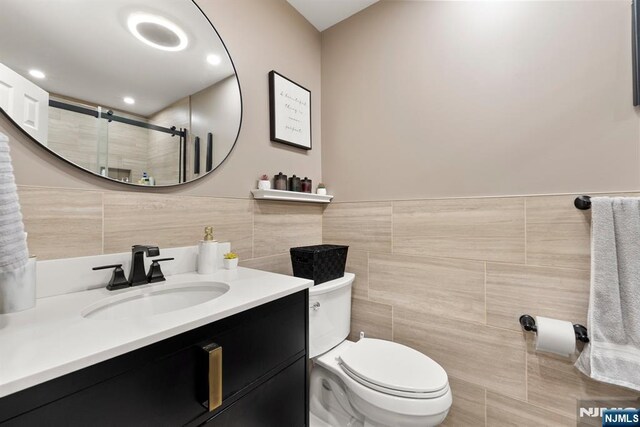 full bath with wainscoting, vanity, toilet, tile walls, and a shower stall