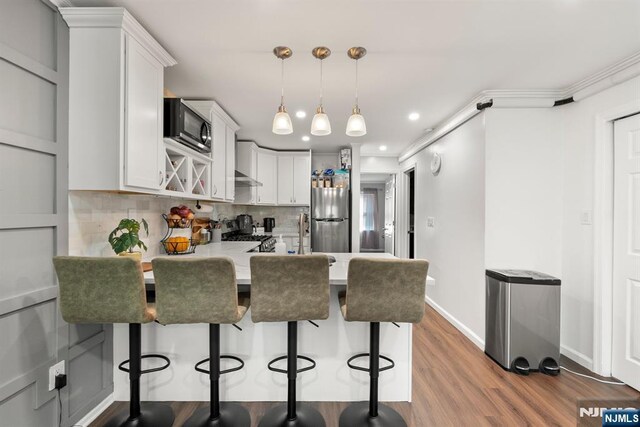 kitchen featuring gas stove, light countertops, freestanding refrigerator, a peninsula, and wood finished floors