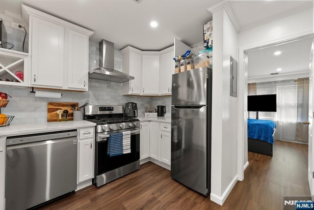 kitchen featuring wall chimney exhaust hood, appliances with stainless steel finishes, white cabinetry, and tasteful backsplash