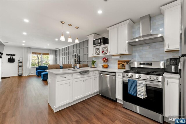 kitchen with wall chimney range hood, light countertops, a peninsula, open floor plan, and stainless steel appliances