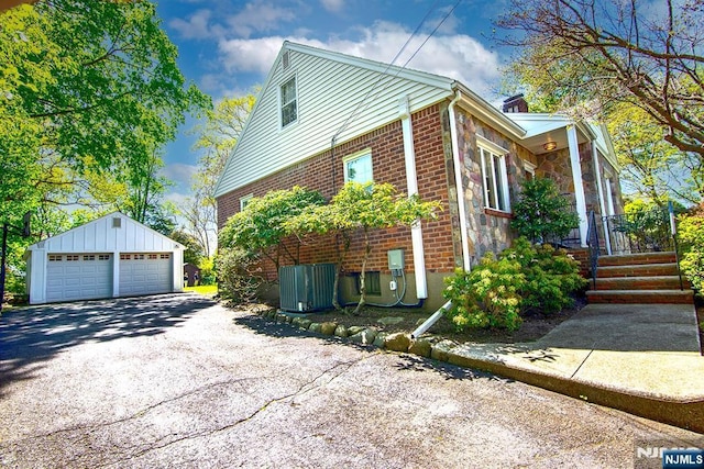 view of home's exterior with stone siding, central AC unit, an outdoor structure, brick siding, and a detached garage