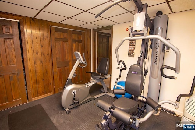 workout area featuring a drop ceiling and wood walls
