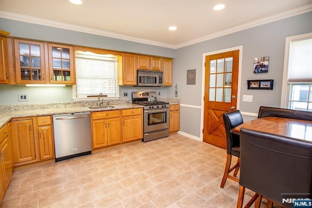 kitchen with light stone countertops, glass insert cabinets, ornamental molding, a sink, and appliances with stainless steel finishes