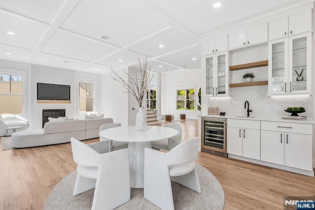 dining room featuring light wood-style flooring, wet bar, wine cooler, and coffered ceiling