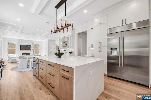 kitchen featuring hanging light fixtures, white cabinets, beamed ceiling, stainless steel appliances, and light wood-style flooring