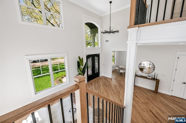 entrance foyer featuring french doors, a towering ceiling, crown molding, wood finished floors, and a notable chandelier
