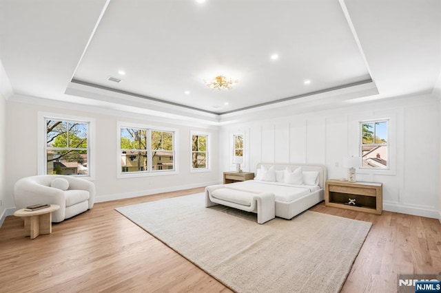 bedroom with recessed lighting, a tray ceiling, multiple windows, and light wood-type flooring