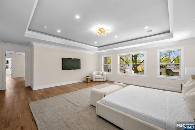 bedroom with crown molding, a tray ceiling, baseboards, and wood finished floors