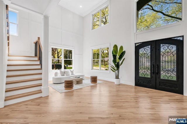 foyer entrance with french doors, wood finished floors, a high ceiling, stairs, and a wealth of natural light