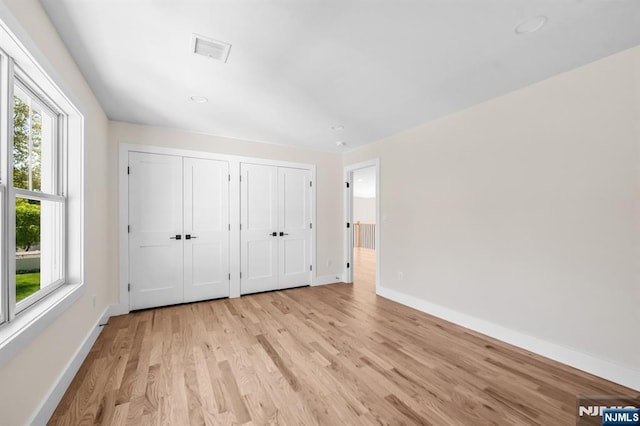unfurnished bedroom featuring multiple closets, visible vents, baseboards, and light wood-style flooring