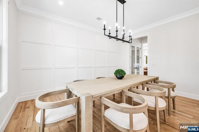 dining area with crown molding, baseboards, a decorative wall, and light wood-type flooring