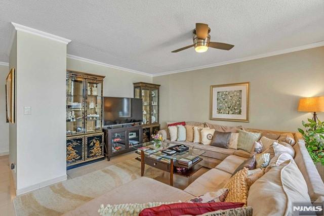 living area featuring ceiling fan, ornamental molding, and a textured ceiling