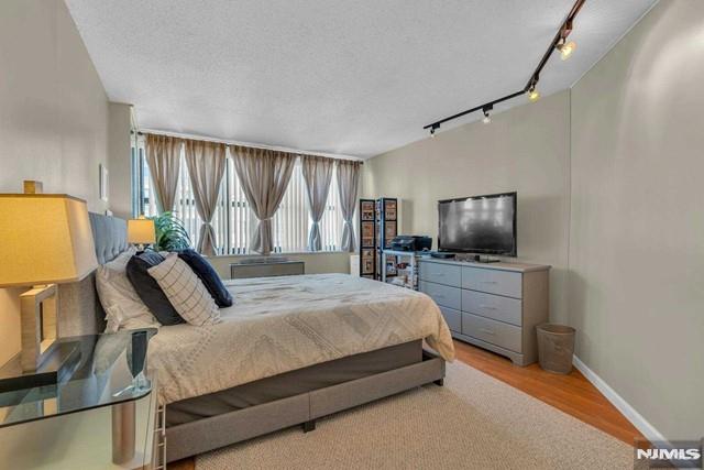 bedroom with a textured ceiling, baseboards, track lighting, and wood finished floors