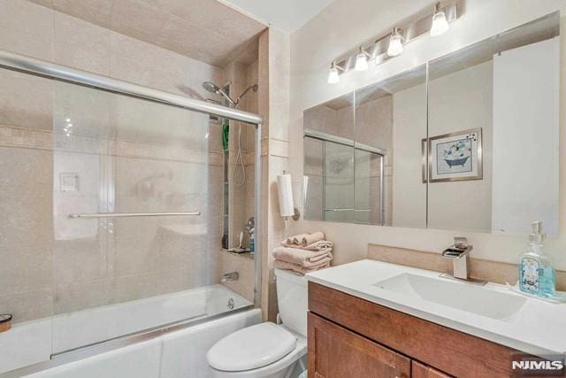 bathroom featuring vanity, combined bath / shower with glass door, and toilet