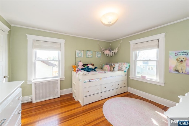 bedroom with light wood-style floors, ornamental molding, radiator heating unit, and multiple windows