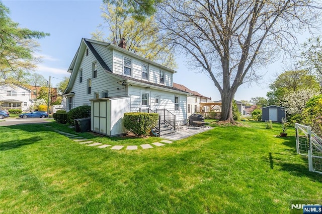 rear view of property featuring a storage shed, an outdoor structure, a chimney, and a lawn