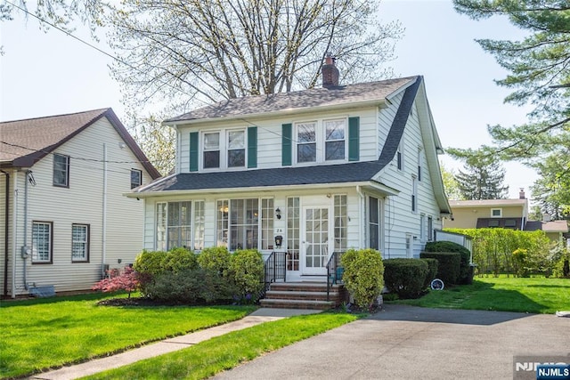 view of front of house with a shingled roof, a front lawn, and a chimney
