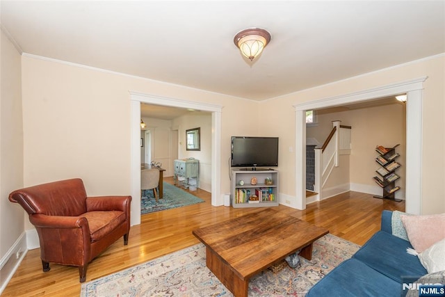 living area featuring baseboards, ornamental molding, wood finished floors, and stairway
