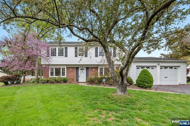 colonial inspired home featuring brick siding, an attached garage, a front yard, and aphalt driveway