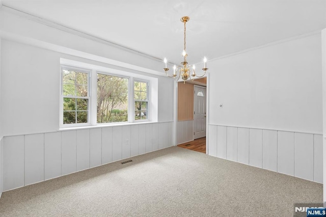 carpeted empty room with an inviting chandelier, wainscoting, and visible vents