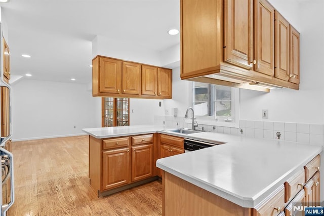 kitchen with light countertops, a peninsula, a sink, and light wood-style flooring