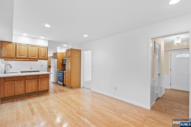 kitchen featuring appliances with stainless steel finishes, a sink, light wood-style floors, light countertops, and brown cabinetry