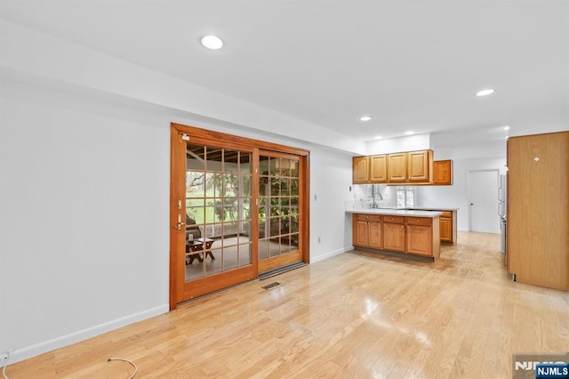 kitchen with light countertops, baseboards, a sink, recessed lighting, and light wood-style flooring