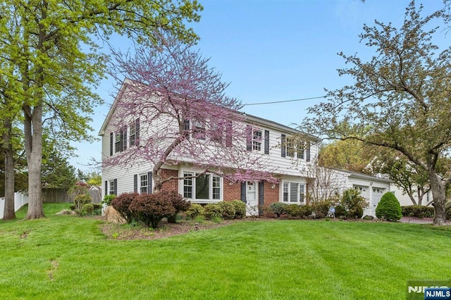 colonial house featuring fence, an attached garage, a front lawn, and brick siding