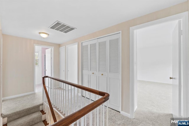 hall with visible vents, carpet, baseboards, and an upstairs landing