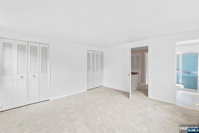 unfurnished bedroom featuring carpet floors, multiple closets, ensuite bath, and baseboards