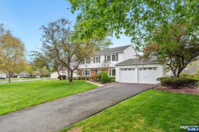 colonial home featuring a garage, a front lawn, aphalt driveway, and roof with shingles