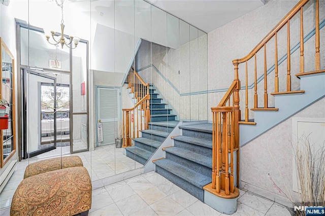 staircase featuring marble finish floor, a notable chandelier, and baseboard heating