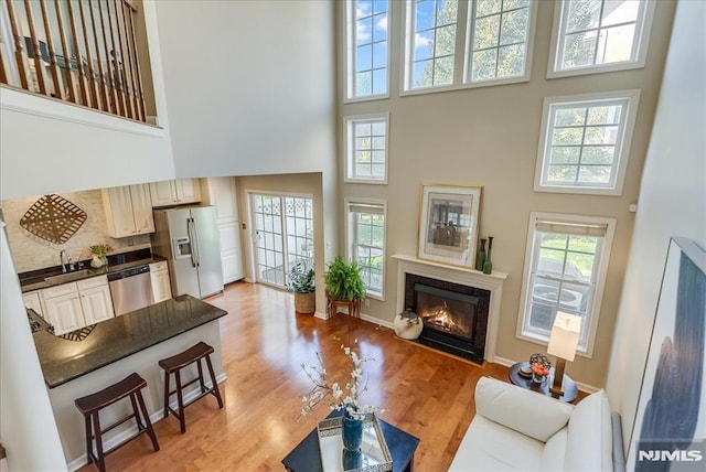 living area with plenty of natural light, a high ceiling, light wood-style floors, and a premium fireplace