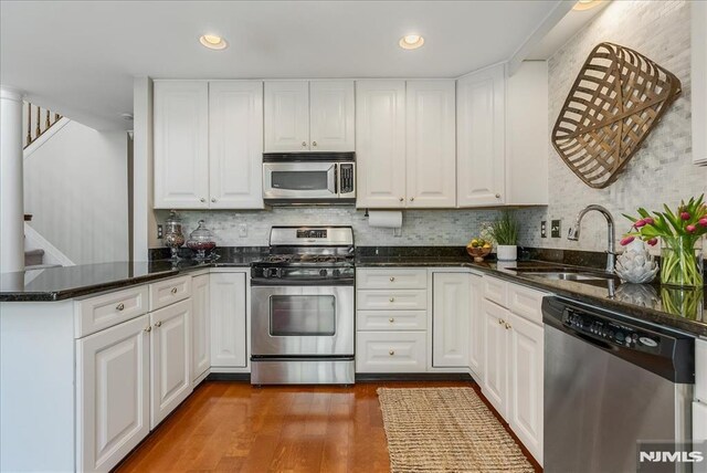 kitchen with white cabinets, appliances with stainless steel finishes, a sink, a peninsula, and wood finished floors
