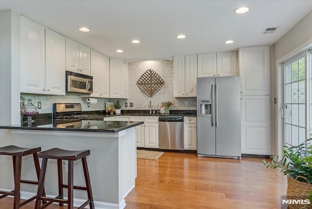 kitchen with visible vents, a peninsula, white cabinetry, light wood finished floors, and stainless steel appliances