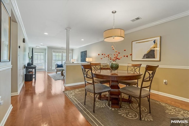 dining area with decorative columns, visible vents, crown molding, a wood stove, and wood-type flooring